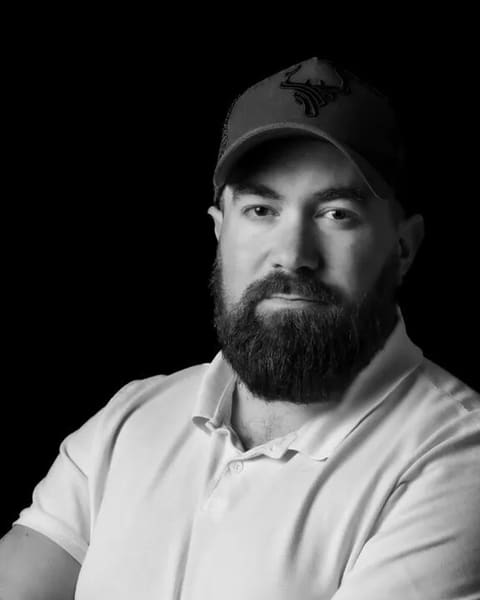 Kevin Machy, portrait en noir et blanc sur fond noir, bras croisés