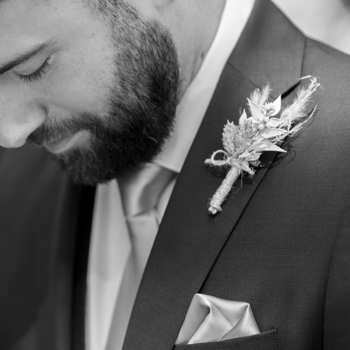 Le marié baisse les yeux vers sa boutonnière, en noir et blanc.