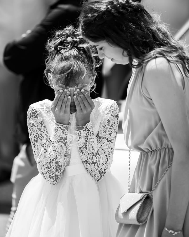 Une enfant cache son visage dans ses mains pendant la cérémonie, en noir et blanc.