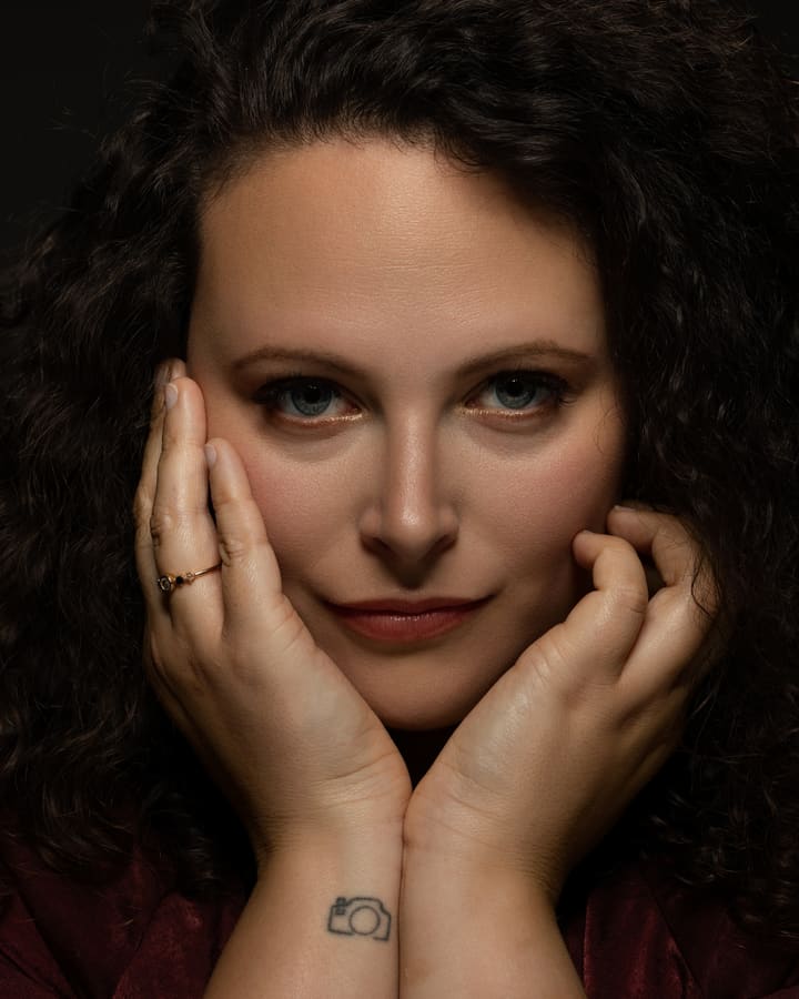 Portrait de face, les deux mains encadrant le visage, sur fond sombre.