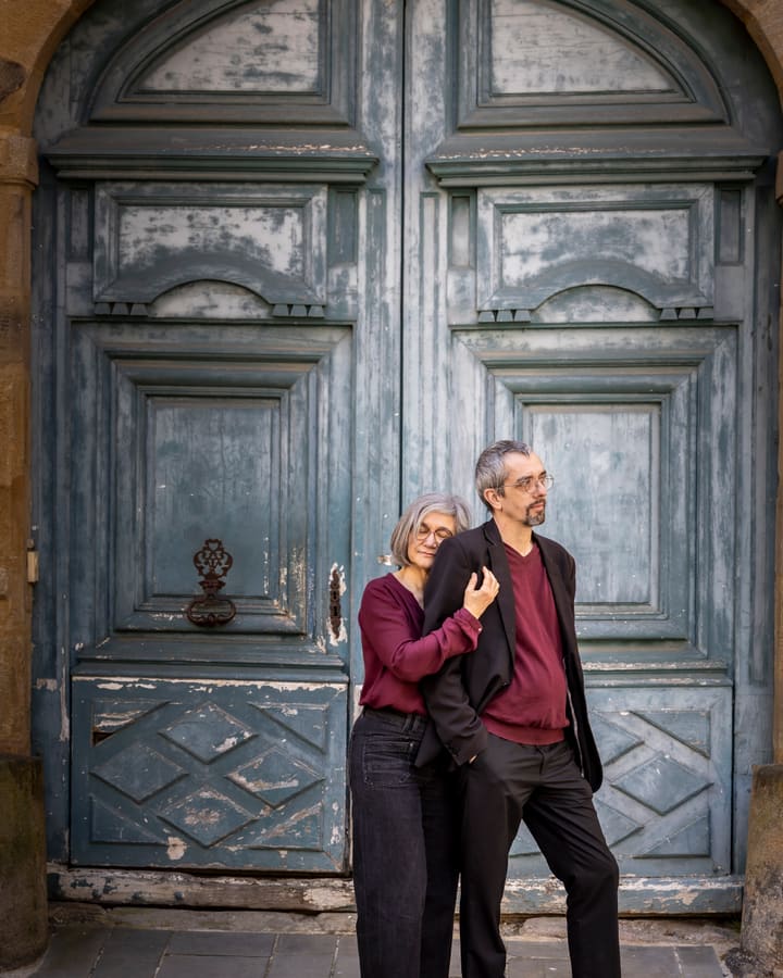 Un couple enlacé devant une grande porte de bois peinte en bleu.